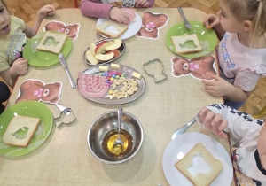 dzieci z grupy maluszków siedzą przy stoliku i jedzą chleb w kształci misia