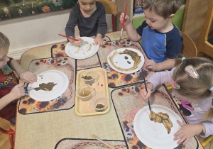 dzieci z grupy maluchów malują głowę misia na talerzyku papierowym