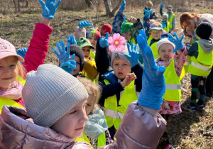 Dzieci idą parami z workami na śmieci i pokazują założone niebieskie gumowe rękawiczki, są gotowe do sprzątania świata.