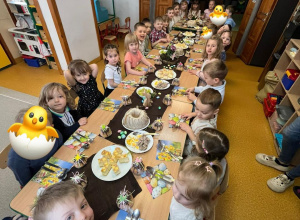 Dzieci siedzą przy zastawionym, świątecznym stole. Przygotowują się do uroczystego obiadu wielkanocnego