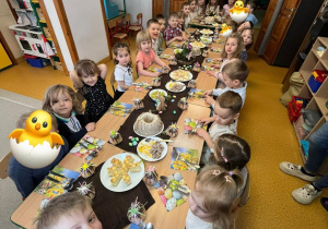 Dzieci siedzą przy zastawionym, świątecznym stole. Przygotowują się do uroczystego obiadu wielkanocnego