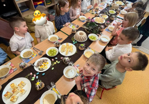 Dzieci siedzą przy zastawionym, świątecznym stole. Przygotowują się do uroczystego obiadu wielkanocnego