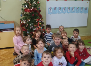 dzieci z grupy Średniaków pozują w świątecznych strojach na tle choinki.