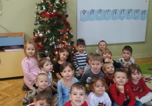 dzieci z grupy Średniaków pozują w świątecznych strojach na tle choinki.