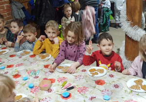 dzieci siedzą przy stołach wyłożonych ceratą i ozdabiają trzy pierniczki