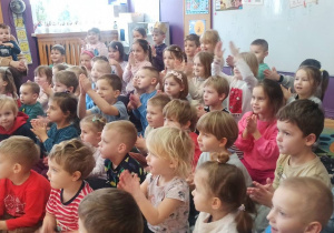 Wszystkie dzieci z przedszkola siedzą na dywanie i z zaciekawienie obserwują iluzjonistę