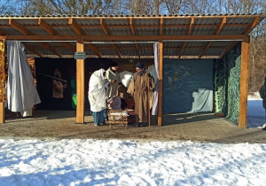 Dzieci siedzą na widowni na dworze, zamiast sceny jest altanka drewniana. Podopieczni przedstawiają jasełka. Na zdjęciu jest zimowa aura