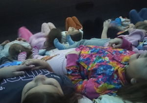 Dzieci leżą na poduszkach w kopule kina sferycznego i oglądają bajkę
