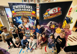 Dzieci pozują na tle dwóch plakatów Polskiego Planetarium Astronomicznego
