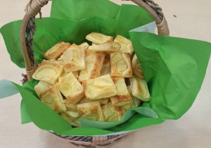Zdjęcie przedstawia upieczone przez dzieci ciasteczka jabłkowe w koszyku na zielonej serwecie
