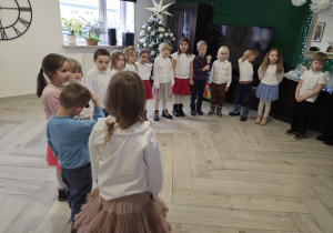 Dzieci stoją w półkolu ubrane na galowo i śpiewają piosenkę