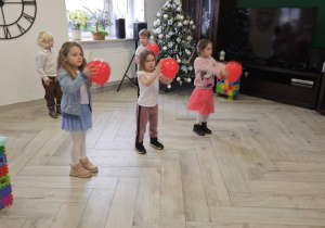 Dziewczynki stoją z czerwonymi balonami, w tle stoi choinka