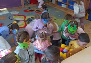 Dzieci mają na twarzy kolorowe maski dinozaurów i szukają kolorowych kulek, które mają być jajami dinozaura