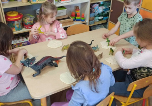 dzieci siedzą przy stoliku, odbijają ślady dinozaurów w ciastolinie