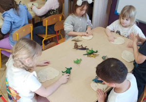 dzieci siedzą przy stoliku, odbijają ślady dinozaurów w ciastolinie