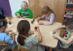 dzieci siedzą przy stoliku, odbijają ślady dinozaurów w ciastolinie