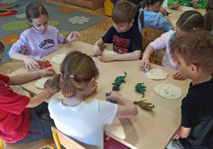 dzieci siedzą przy stoliku, odbijają ślady dinozaurów w ciastolinie