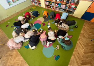 dzieci w kręgu zwinęły się w kulki i udają jajko dinozaura z którego wykluwa się mały dinozaur