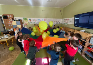 dzieci bawią się chustą animacyjną i zielonymi balonami