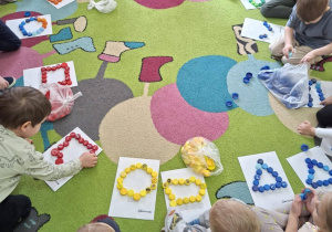Dzieci z kolorowych korków plastikowych układają figury geometryczne
