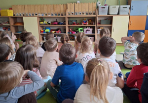 Dzieci siedzą na dywanie tyłem do obiektywu i oglądają film edukacyjny o wodzie