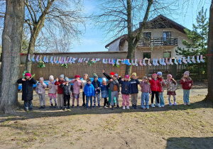 Dzieci stoją w ogrodzie między drzewami, a nad nimi są rozwieszone pokolorowane kolorowe skarpetki