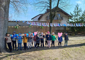 Dzieci stoją w ogrodzie między drzewami, a nad nimi są rozwieszone pokolorowane kolorowe skarpetki