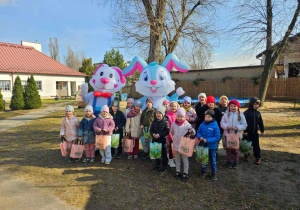 Dzieci ze starszaków pozują w ogrodzie do zdjęcia grupowego wraz z dwoma dużymi królikami