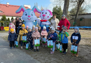 Dzieci ze maluszków pozują w ogrodzie do zdjęcia grupowego wraz z dwoma dużymi królikami