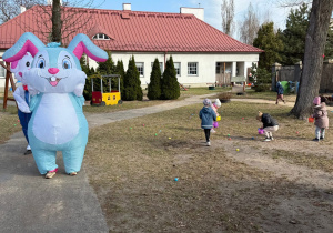 Człowiek w dużym stroju królika ukrywa jej czka przed dziećmi, dzieci w ogrodzie szukają ukrytych jajek.