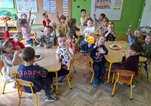 Dzieci siedzą przy stolikach, tworzą szaszłyki owocowe.