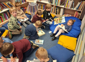 Dzieci siedzą w przestrzeni biblioteki na kanapach i poduchach i swobodnie oglądają książki