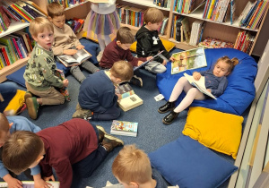 Dzieci siedzą w przestrzeni biblioteki na kanapach i poduchach i swobodnie oglądają książki