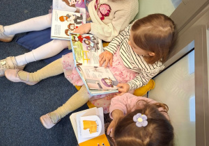 Trzy dziewczynki siedzą na poduchach i oglądają wybrane przez siebie książki