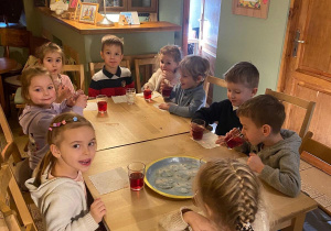 Dzieci siedzą przy dębowych stolikach i korzystają z poczęstunku.