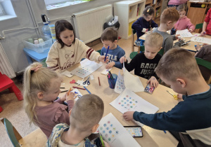 Dzieci siedzą przy stoliku i tworzą z papieru kolorowe telefony komórkowe