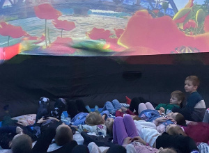 Dzieci leżą na poduszkach pod kopułą kina sferycznego i oglądają film edukacyjny o porach roku.