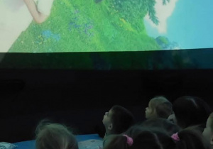 Dzieci leżą na poduszkach pod kopułą kina sferycznego i oglądają film edukacyjny o porach roku.