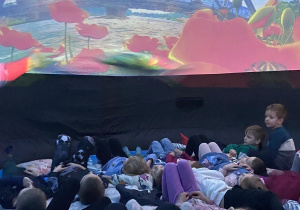 Dzieci leżą na poduszkach pod kopułą kina sferycznego i oglądają film edukacyjny o porach roku.