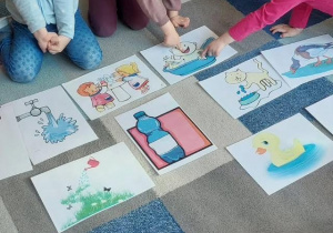 Dzieci siedzą na dywanie i oglądają kardy edukacyjne związane z tematem Dnia Wody