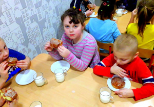 Dzieci z najstarszej grupy siedzą przy stoliku w jadalni i jedzą pączki.
