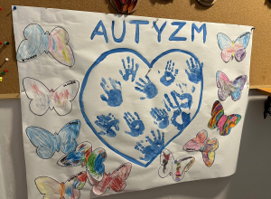 Zdjęcie przedstawia grupową prace plastyczną dzieci z grupy maluszków. Na pracy widnieje niebieskie serce, w którym odciśnięte są dłonie dzieci, a wokół naklejone są pokolorowane motyle