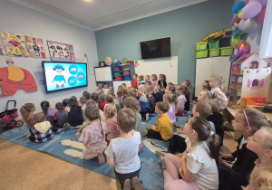 Dzieci siedzą na dywanie i oglądają film edukacyjny dotyczący bezpieczeństwa