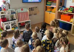 Dzieci siedzą na dywanie przed i oglądają film edukacyjny dotyczący segregacji śmieci