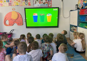 Dzieci siedzą na dywanie przed i oglądają film edukacyjny dotyczący segregacji śmieci