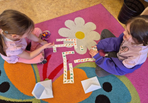 Dwie dziewczynki układają domino w temacie Dnia Ziemi na dywanie