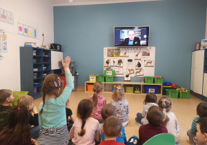 Dzieci siedzą na podłodze przed telewizorem i uczestniczą w spotkaniu przez teamsy z Panem z Grupowej Oczyszczalni Ścieków w Łodzi.