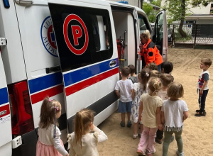 Zdjęcie przedstawia ambulans który jest na terenie przedszkola. Ratownik medyczny zapoznaje dzieci z tym jak wygląda ambulans od środka.