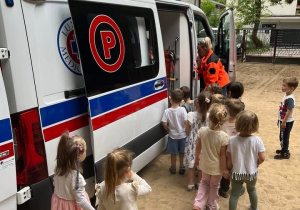 Zdjęcie przedstawia ambulans który jest na terenie przedszkola. Ratownik medyczny zapoznaje dzieci z tym jak wygląda ambulans od środka.