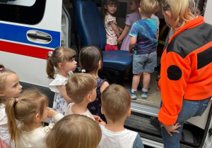 Zdjęcie przedstawia ambulans który jest na terenie przedszkola. Ratownik medyczny zapoznaje dzieci z tym jak wygląda ambulans od środka.